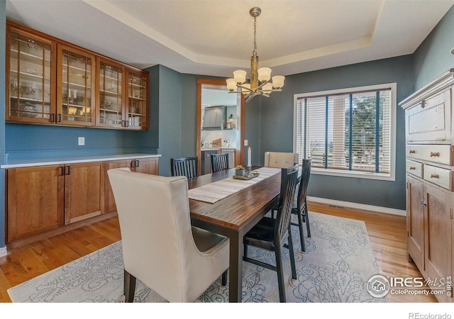 dining space featuring a raised ceiling, baseboards, a notable chandelier, and light wood finished floors