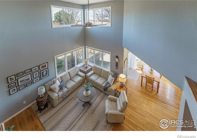 living room with ceiling fan, a high ceiling, wood finished floors, and baseboards