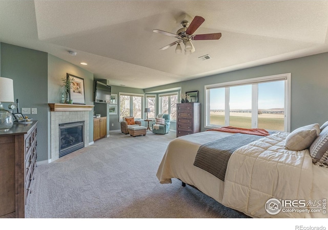 bedroom with ceiling fan, light colored carpet, visible vents, baseboards, and a tiled fireplace