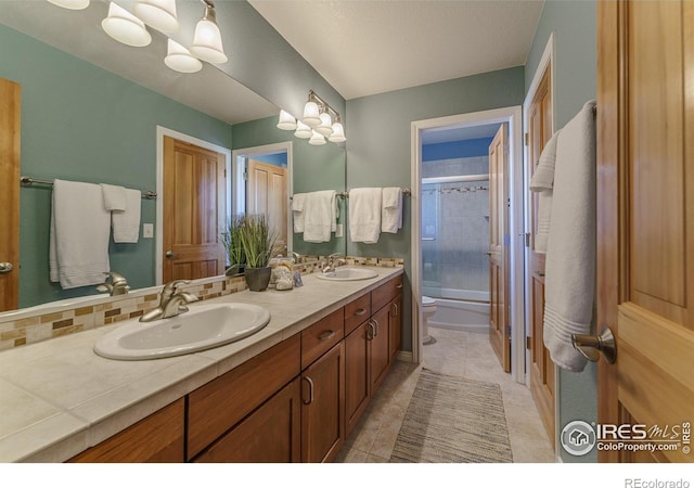 bathroom featuring toilet, double vanity, enclosed tub / shower combo, and a sink