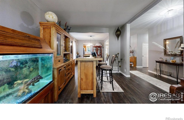 kitchen featuring glass insert cabinets, brown cabinets, a center island, hanging light fixtures, and a kitchen bar