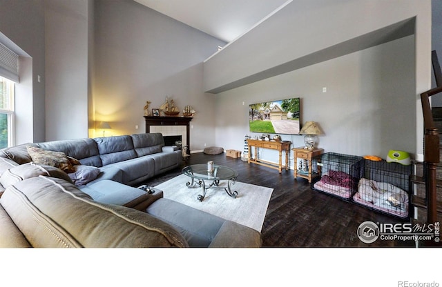 living room featuring high vaulted ceiling, a tile fireplace, baseboards, and wood finished floors