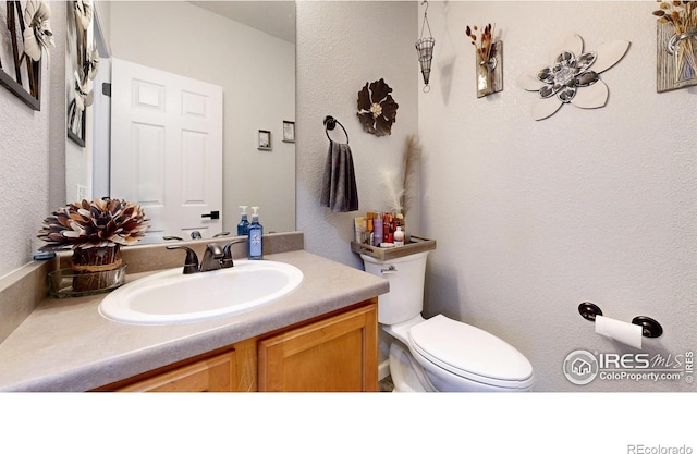 bathroom featuring toilet, a textured wall, and vanity