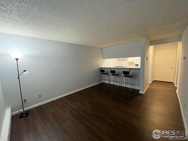 unfurnished living room with dark wood-style floors, a textured ceiling, and baseboards