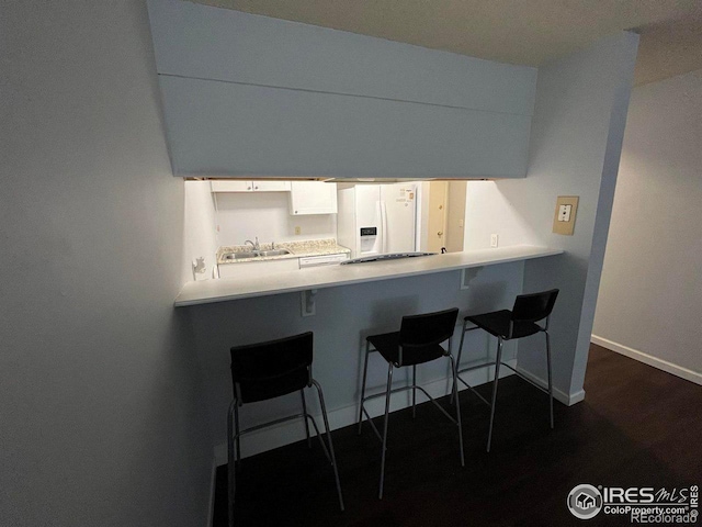 kitchen featuring a peninsula, white refrigerator with ice dispenser, a breakfast bar, a sink, and light countertops