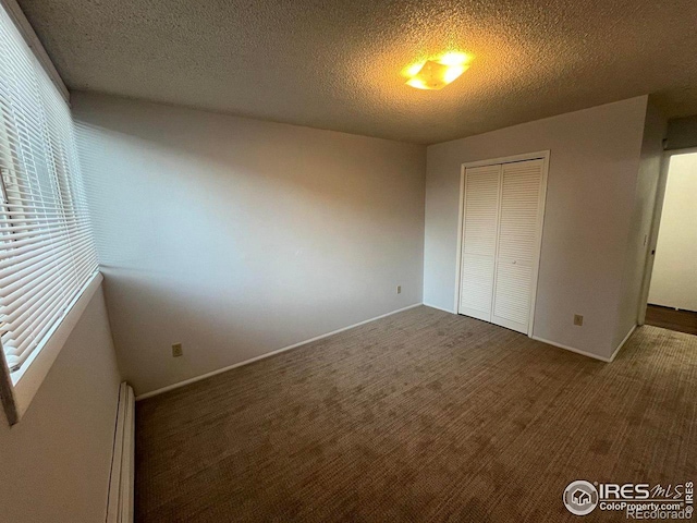 unfurnished bedroom featuring a textured ceiling, a baseboard heating unit, baseboards, a closet, and dark carpet