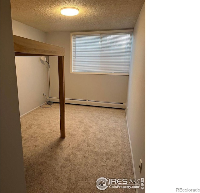 finished below grade area with light carpet, baseboard heating, and a textured ceiling