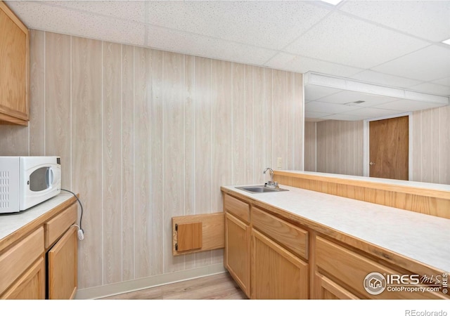 kitchen with white microwave, a paneled ceiling, a sink, light countertops, and light wood-type flooring