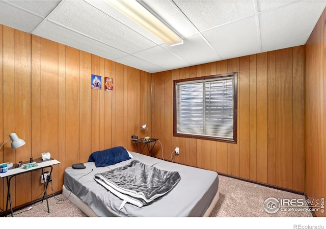 bedroom with light colored carpet, wood walls, and a drop ceiling