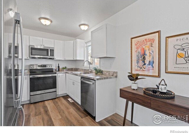 kitchen featuring dark wood-style flooring, stainless steel appliances, light countertops, white cabinetry, and a sink