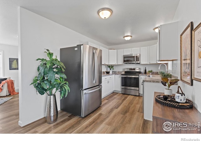 kitchen with appliances with stainless steel finishes, a sink, light wood-style flooring, and white cabinets