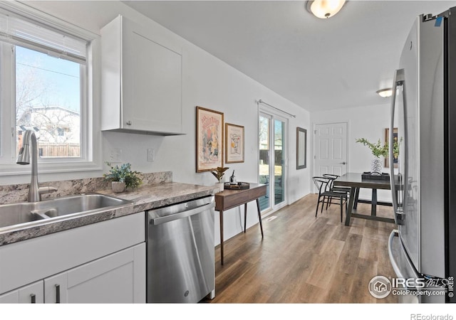 kitchen with appliances with stainless steel finishes, white cabinets, a sink, and wood finished floors