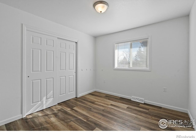 unfurnished bedroom with a closet, visible vents, dark wood finished floors, and baseboards