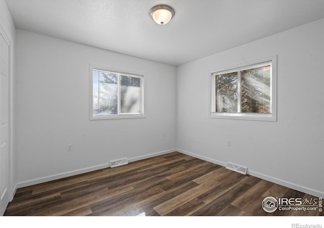 unfurnished room featuring dark wood finished floors, visible vents, and baseboards