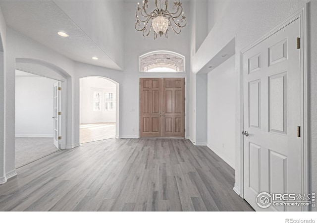 entrance foyer with arched walkways, a chandelier, wood finished floors, a towering ceiling, and baseboards