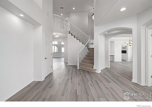 foyer entrance with baseboards, visible vents, arched walkways, and wood finished floors