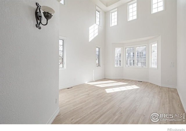 unfurnished living room with a high ceiling, light wood-type flooring, visible vents, and baseboards