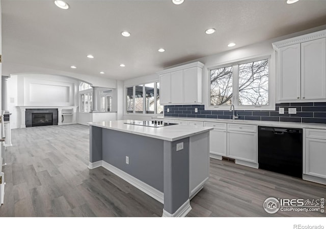 kitchen with black appliances, tasteful backsplash, a kitchen island, and ornate columns