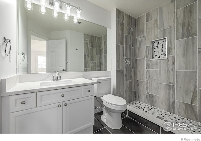 bathroom featuring toilet, tile patterned flooring, a tile shower, and vanity