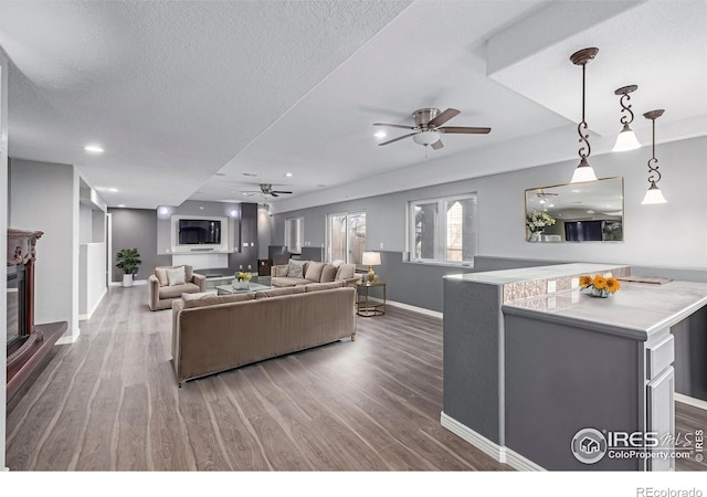 living room with a ceiling fan, a glass covered fireplace, a textured ceiling, and wood finished floors