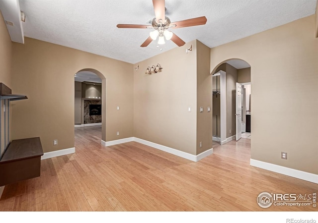 empty room with light wood-style floors, arched walkways, a textured ceiling, and baseboards