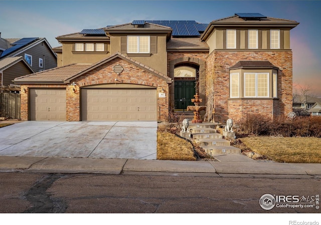 view of front of house featuring stucco siding, driveway, an attached garage, solar panels, and a tiled roof