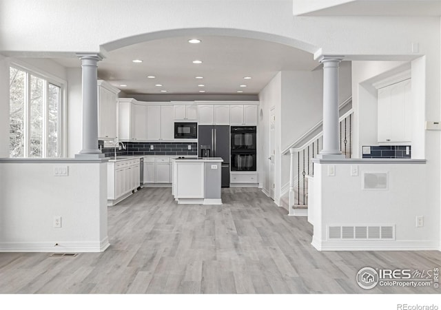 kitchen with a sink, visible vents, white cabinetry, backsplash, and black appliances