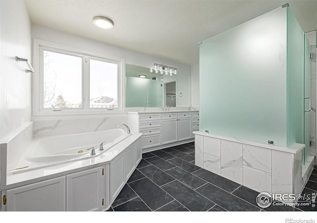 bathroom featuring a stall shower, a jetted tub, vanity, and a textured ceiling