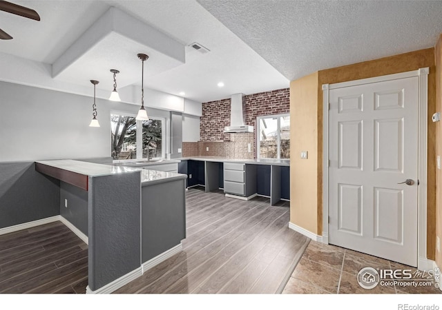 kitchen with wood finished floors, light countertops, wall chimney range hood, and hanging light fixtures