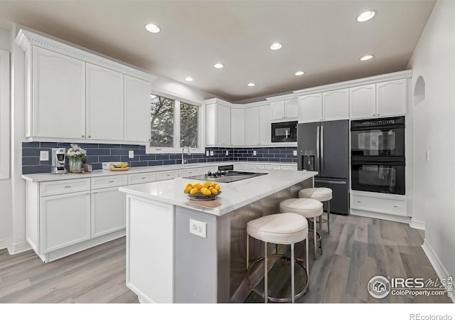 kitchen with decorative backsplash, black appliances, a breakfast bar, and white cabinetry