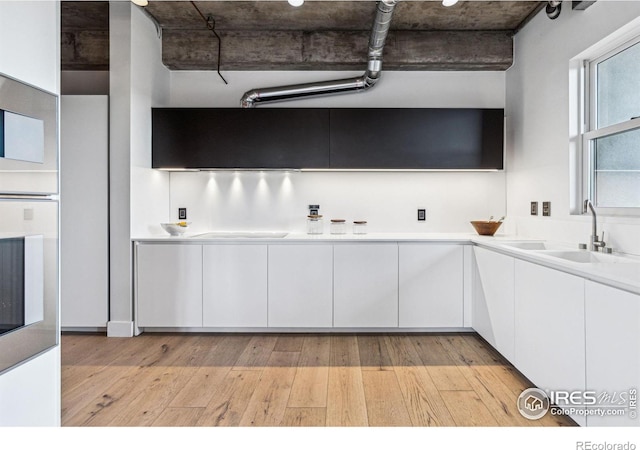 kitchen with light countertops, white cabinets, a sink, modern cabinets, and light wood-type flooring