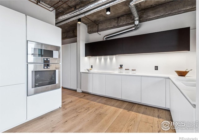 kitchen with double oven, light wood-style floors, white cabinets, light countertops, and modern cabinets