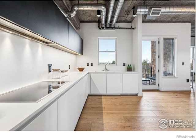 kitchen with black electric cooktop, a sink, visible vents, white cabinetry, and light countertops