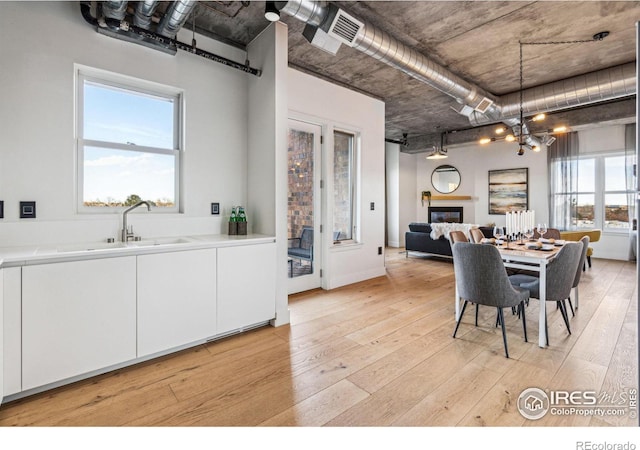 dining space with a glass covered fireplace, visible vents, light wood-style flooring, and an inviting chandelier