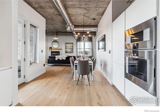 dining room with a glass covered fireplace, light wood-style flooring, and baseboards