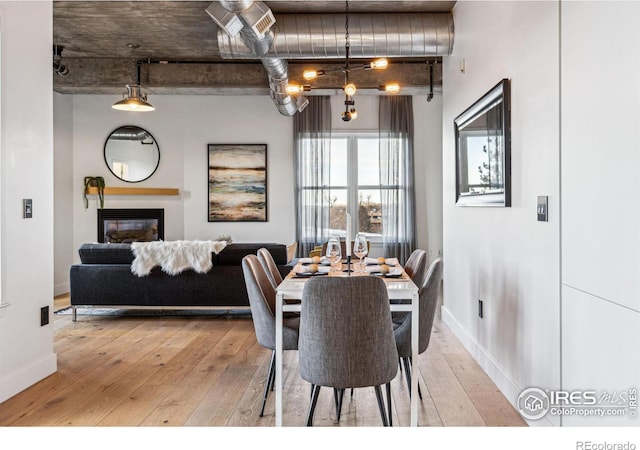 dining space featuring light wood-type flooring, a glass covered fireplace, and baseboards