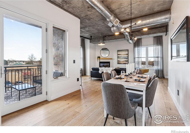 dining area featuring baseboards, light wood-type flooring, a glass covered fireplace, and an inviting chandelier