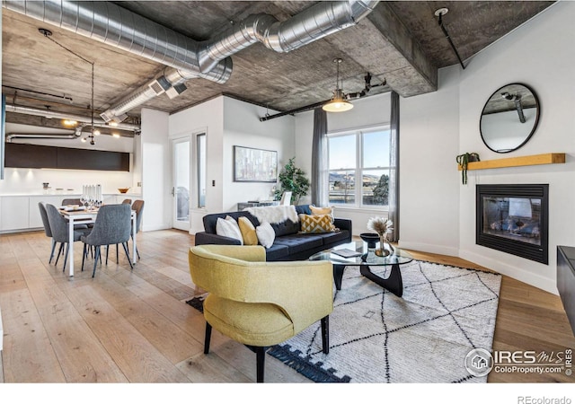 living room featuring light wood-style flooring, baseboards, and a glass covered fireplace