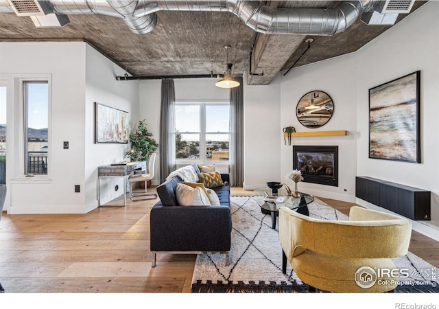 living room with a glass covered fireplace, baseboards, visible vents, and hardwood / wood-style floors