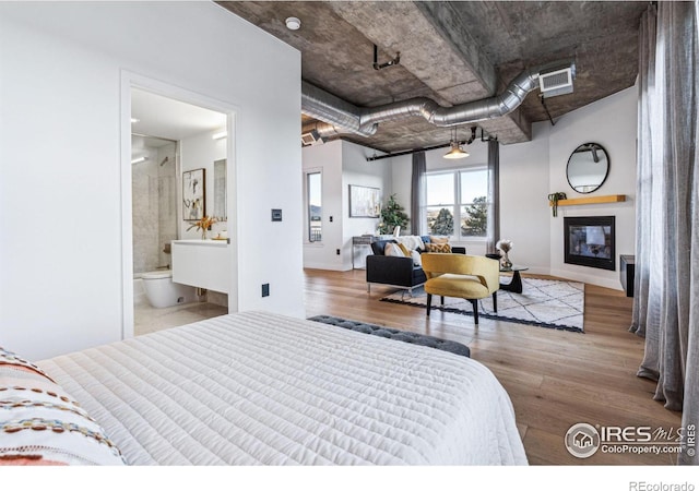 bedroom featuring light wood-style floors, a glass covered fireplace, visible vents, and baseboards