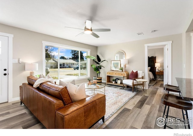 living area with light wood-type flooring, visible vents, ceiling fan, and baseboards