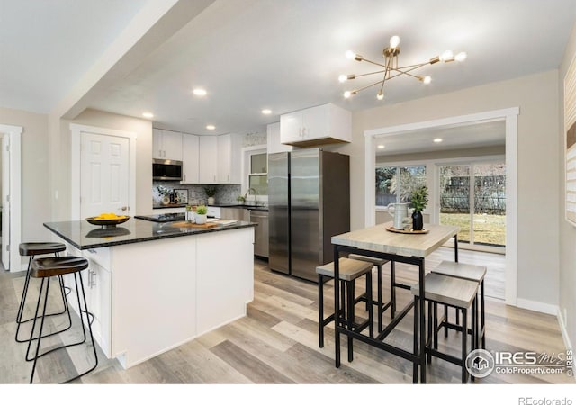 kitchen featuring light wood finished floors, tasteful backsplash, appliances with stainless steel finishes, white cabinetry, and a sink