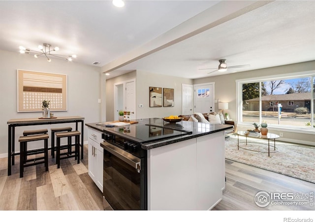 kitchen featuring black range with electric cooktop, light wood-style flooring, a ceiling fan, white cabinetry, and baseboards