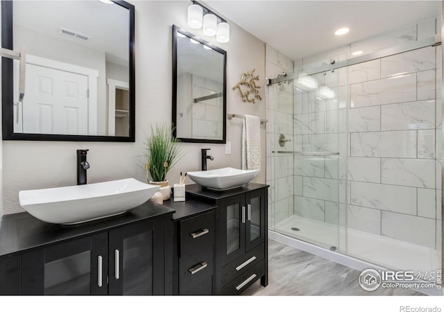 full bath featuring double vanity, a sink, visible vents, and a shower stall