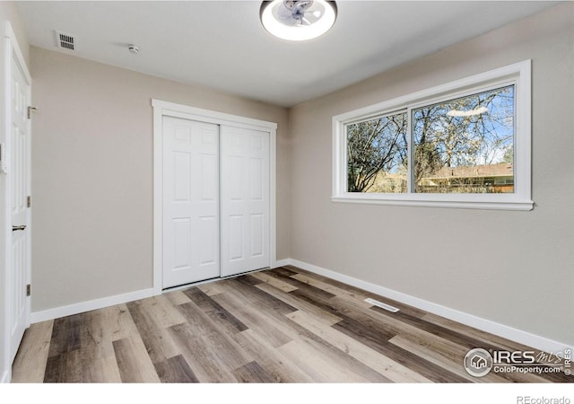 unfurnished bedroom featuring a closet, wood finished floors, visible vents, and baseboards