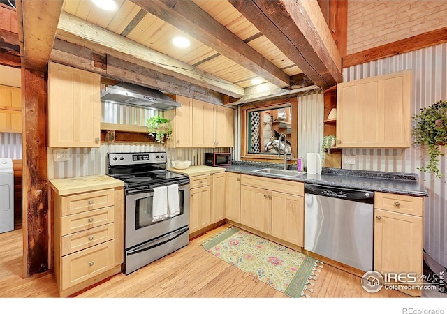 kitchen featuring a sink, appliances with stainless steel finishes, beam ceiling, wall chimney exhaust hood, and washer / dryer