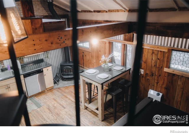 kitchen with dark countertops, light wood-style flooring, a wood stove, wood walls, and stainless steel dishwasher