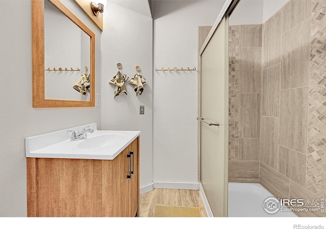 full bathroom featuring tiled shower, vanity, and wood finished floors