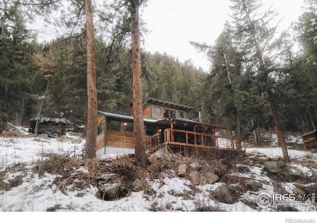 snow covered property featuring a view of trees and a wooden deck