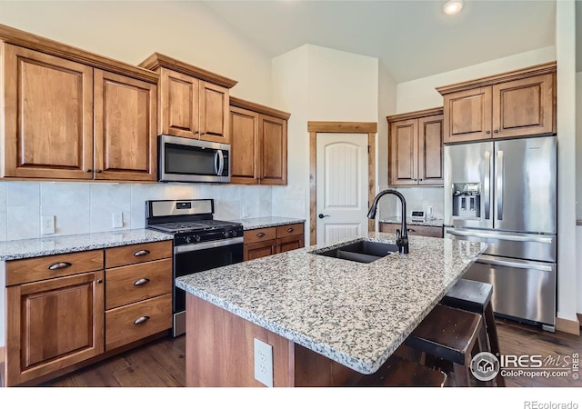 kitchen featuring decorative backsplash, brown cabinetry, appliances with stainless steel finishes, light stone countertops, and a sink